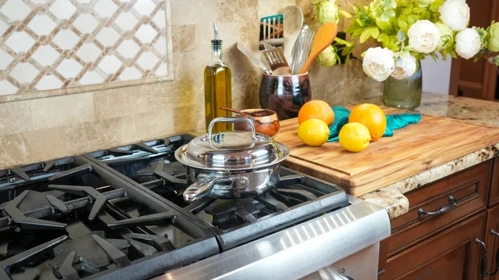 Stainless steel 1-quart saucepan with lid on a gas stove beside a wooden cutting board with oranges and kitchen utensils