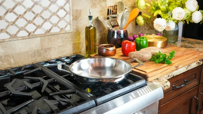 Top-down view of 10-inch stainless steel fry pan showcasing two short handles and brushed interior on a gas stove with a cutting board nearby