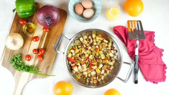 Top-down view of 10-inch stainless steel fry pan with two short riveted handles showcasing cooked breakfast hash and brushed interior on white background