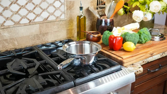 Angled view of 1.75-quart saucepan with cover showing stainless interior and long handle on gas stovetop with cutting board