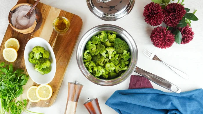 Top-down view of 1.75-qt saucepan filled with broccoli on a white table with a cutting board, lemon slices, and herbs