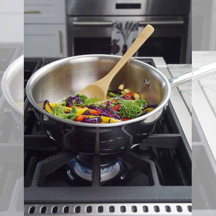 Stainless-steel saucepan on a gas stove with sautéing broccoli, red cabbage and carrots stirred by a wooden spoon