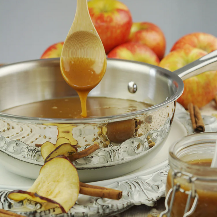 Three-quarter view of 2 quart saucier showing rounded interior and long handle with caramel drizzle and apples behind