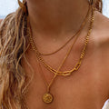 A close-up image of a person wearing a layered gold necklace with a coin pendant, part of the necklace is visible over the person's neckline.