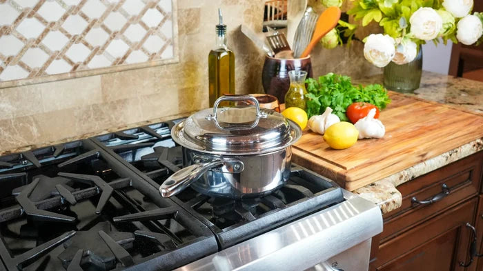 Angled top view of 3-quart stainless steel saucepan with lid showcasing polished interior and long riveted handle on a gas stove