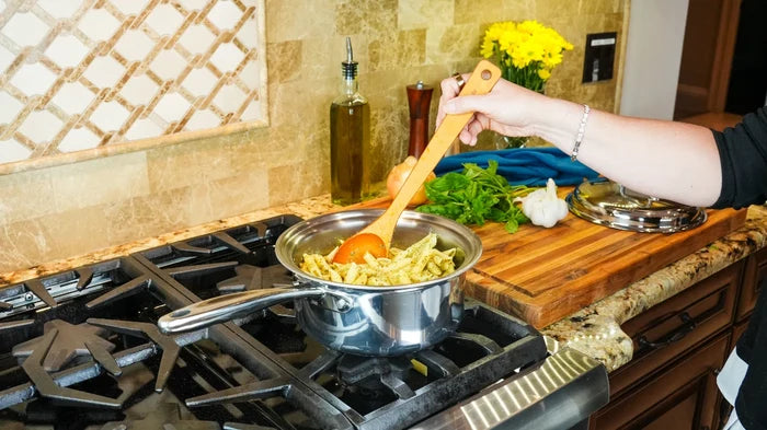 Hand stirring pasta in a 3-quart stainless steel saucepan on a gas stove with wooden spoon and kitchen countertop background