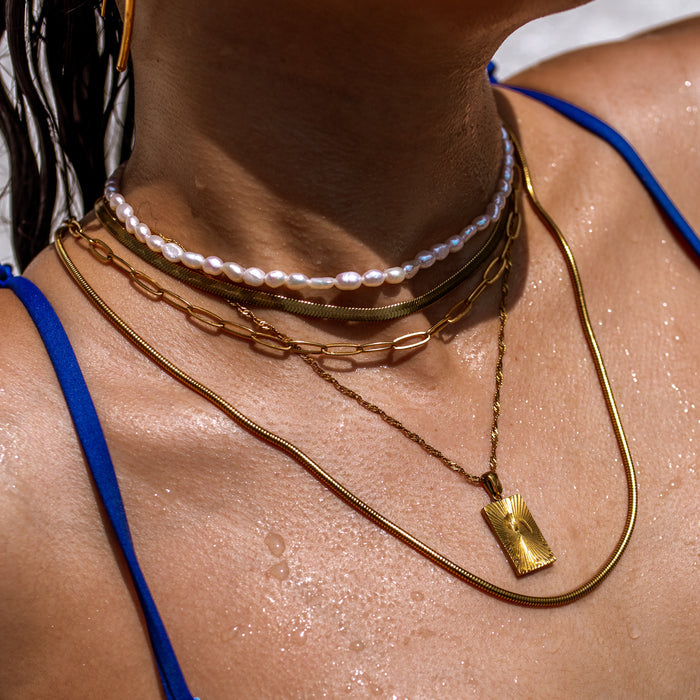 a woman in the pool wearing a waterproof necklace stack by ALCO Jewelry featuring gold chains, pearls and a gold rectangle sunburst pendant