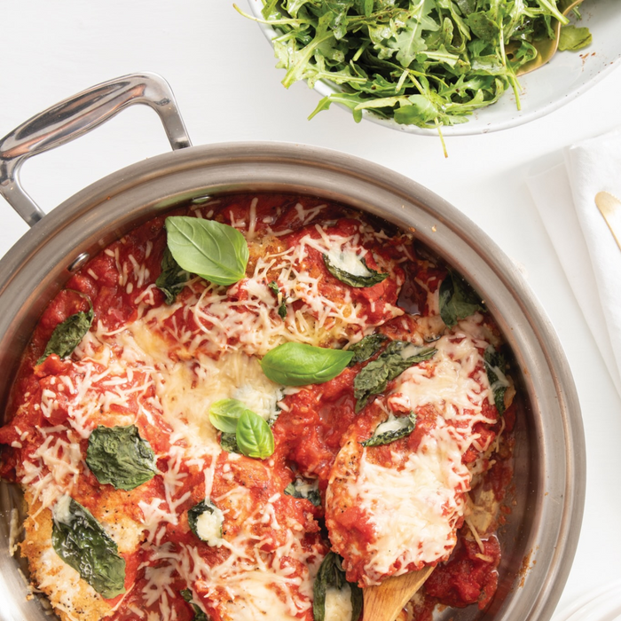 Top view of 3.5-qt stainless steel saute pan with short handles showing chicken Parmesan with basil and salad bowl