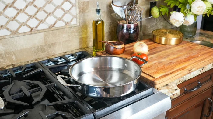 Top-front view of 3.5-qt stainless steel sauté pan with short side handles showing polished interior on gas stove beside cutting board
