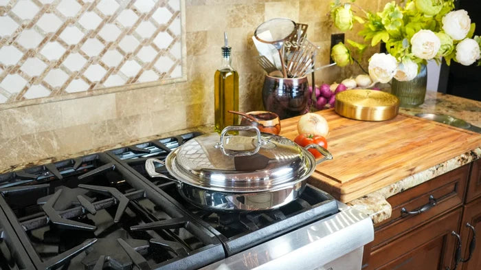Three-quarter view of 3.5-quart stainless steel sauté pan with lid and short handles on a gas stove, wooden cutting board and oil bottle behind