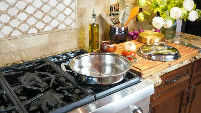 Stainless steel 3.5-quart sauté pan with short handles resting on a gas stove, lid and vegetables on the countertop