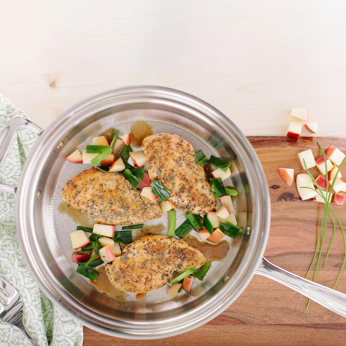 Overhead view of 3.5 Quart Saute Pan showcasing polished stainless steel interior and long handle on a wooden board with cooked chicken