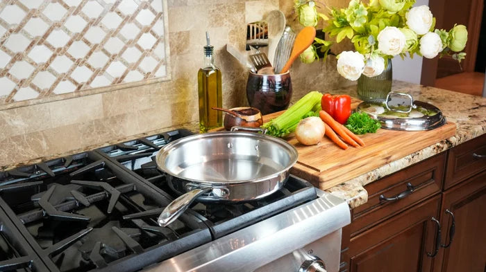 3.5-quart stainless steel sauté pan heating on a gas stove with lid and fresh vegetables on a cutting board nearby in a kitchen