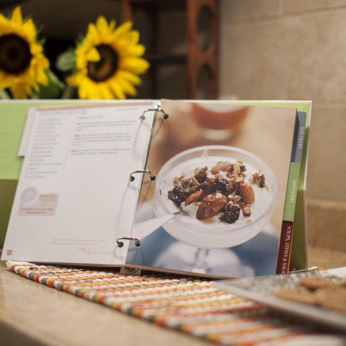 Angled view of 360 Cookbook open to a recipe photo of a bowl with nuts and dried fruit, showing the three-ring binder