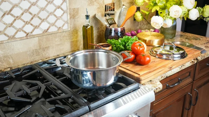 Stainless steel 4-quart stockpot sitting on a gas stovetop with lid and a cutting board of tomatoes and herbs nearby