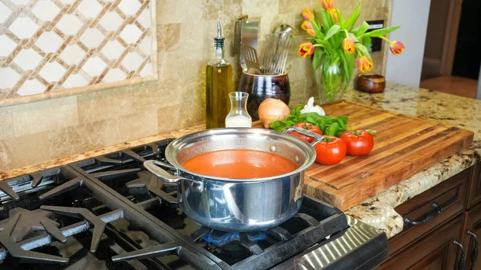 Front angle of 4-quart stainless-steel stockpot showing polished finish and side handles with tomato soup on gas stove
