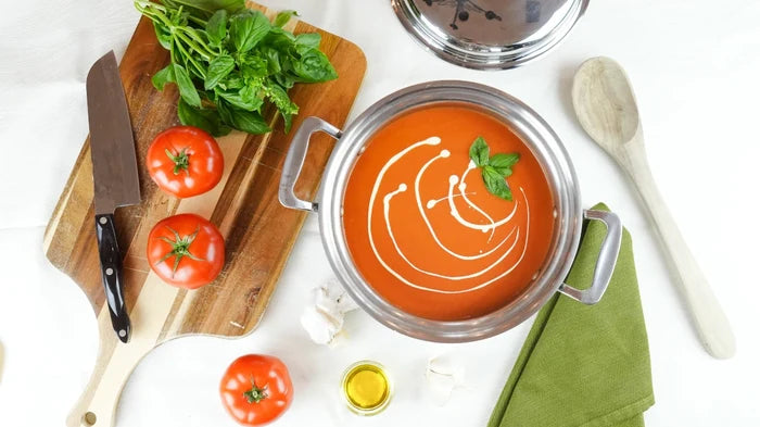 Overhead view of 4-quart stainless steel stockpot with lid and side handles, filled with tomato soup on white surface
