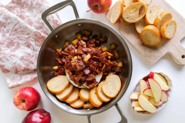 Top-down view of 8.5-inch stainless fry pan with short handles holding cooked apples, bacon, and sliced baguette on white