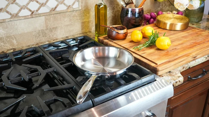 Angled view of 8.5 inch stainless steel fry pan showing polished interior and long riveted handle on a gas stove beside a cutting board with lemons