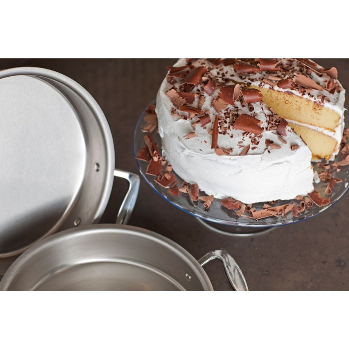 Top-front view of 9” Round Cake Pan with Handles showing brushed stainless finish beside a frosted vanilla cake