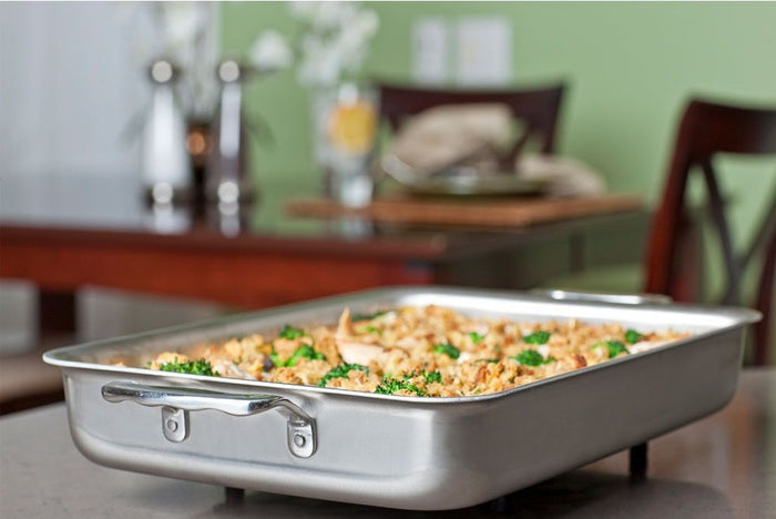 Angled view of 9 x 13 Bake & Roast Pan with Handles showing polished stainless interior and wide side handles with casserole on a dining table