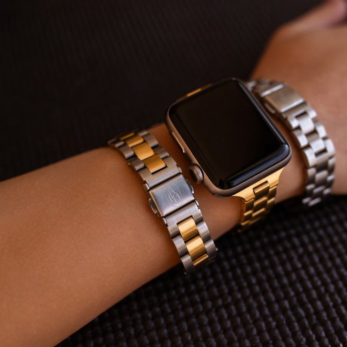 Apple Watch with gold and silver metal band on a wrist against a dark textured fitness mat