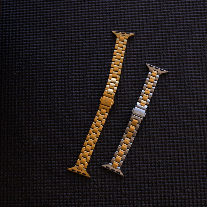 Two waterproof apple watch straps, one gold and one mixed metal, on a textured black fitness mat.