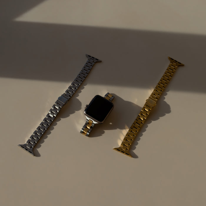 Apple Watch with silver and gold metal bands on a beige surface