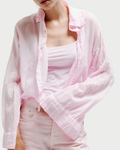 Wearing the All III Daniel Button Down by All III in an oversized, light pink cotton gauze style over a matching pink tank top and high-waisted pink jeans, this woman stands against a neutral background with her face partially out of frame.