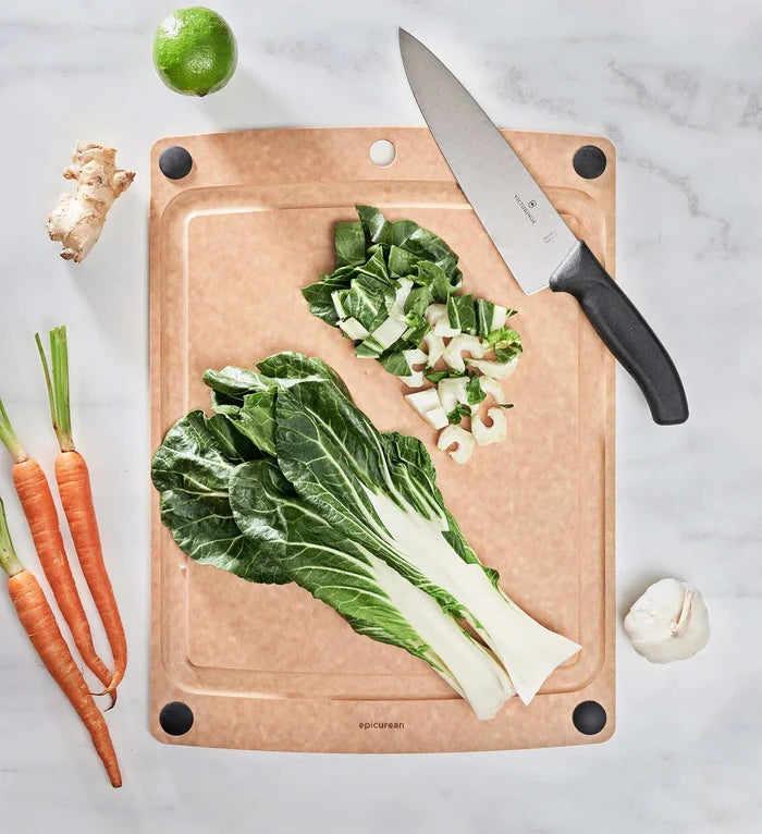Overhead view of All-In-One Series Cutting Board showing juice groove and black non-slip feet with chopped greens and knife on marble