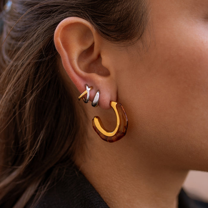 Close-up of an ear wearing a tortoiseshell hoop earring with two mixed metal huggies