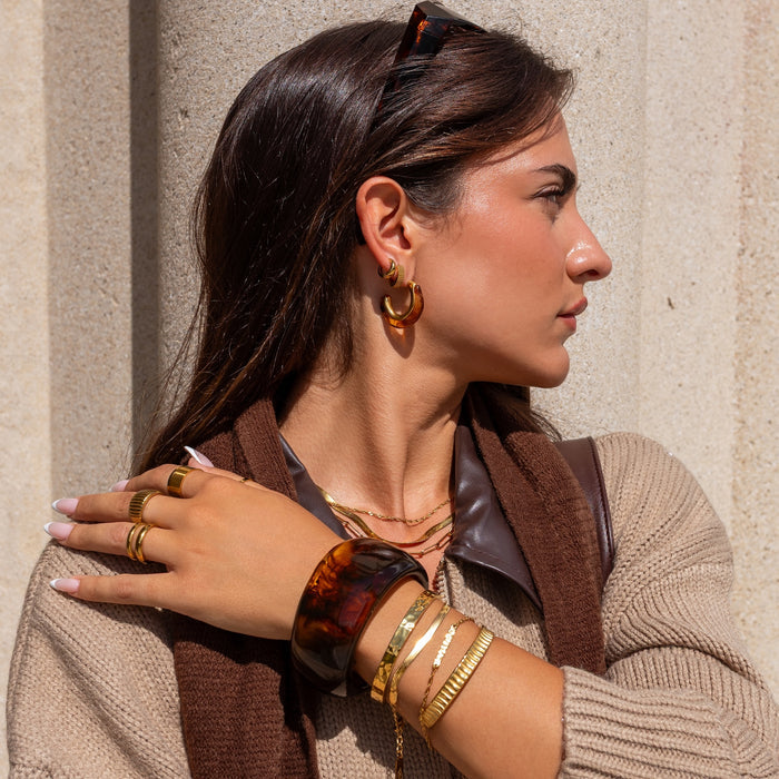 Woman wearing gold and tortoiseshell jewelry against a beige wall
