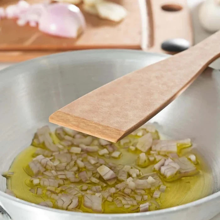 Close up of Angled Turner showcasing flat tapered blade over a stainless steel pan with chopped onions in oil