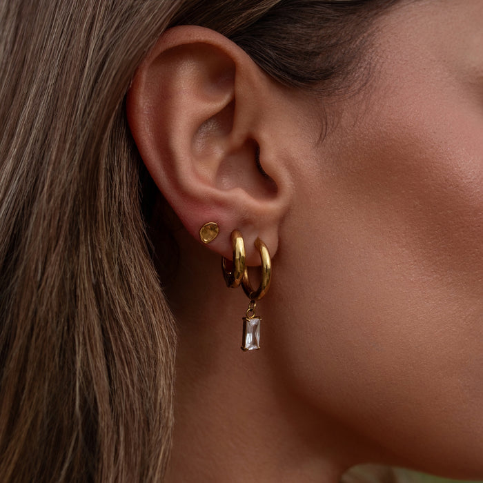 Close-up of an ear wearing gold hoop earrings with a dangling gemstone.