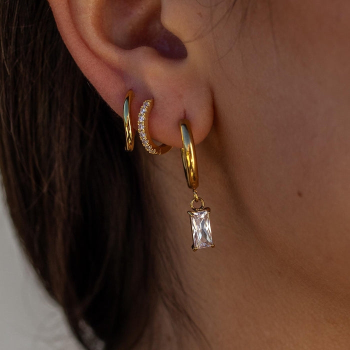 a gemstone earring stack featuring a large huggie with a dangling gemstone, a dainty gemstone huggie, and a smooth wavy gold huggie