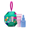 A green, multi-colored ornament-shaped gift box labeled “BYOMA Barrier Boosting Duo,” featuring a pink tube of moisturizing gel-cream and a blue bottle of hydrating serum.   The background is transparent.