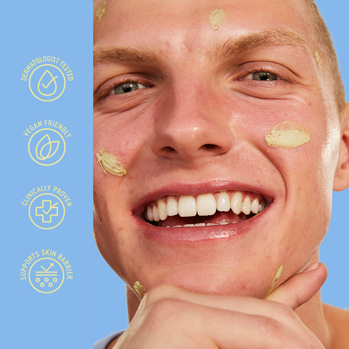 Close-up of a smiling man with beige skincare cream applied to his face against a light blue background, with vertical text icons on the left reading 'Dermatologist Tested', 'Vegan Friendly', 'Clinically Proven', and 'Supports Skin Barrier'.