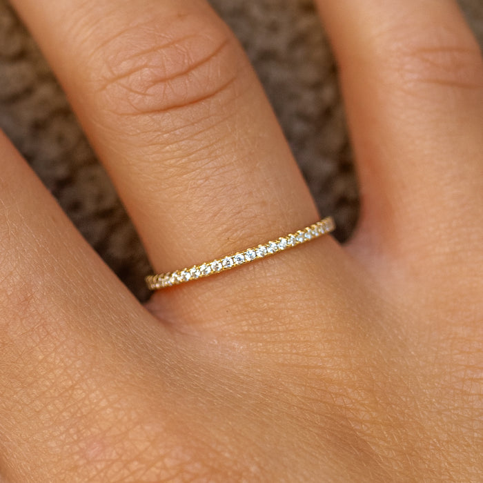 dainty gold ring with small gemstones on a person's finger against a textured brown background