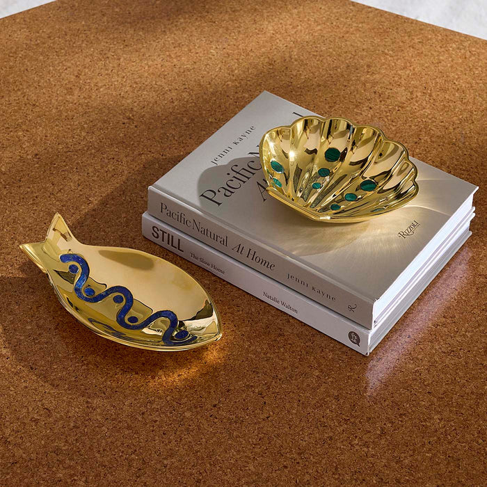 Gold fish and shell-shaped trinket dishes on a stack of books with a brown surface.