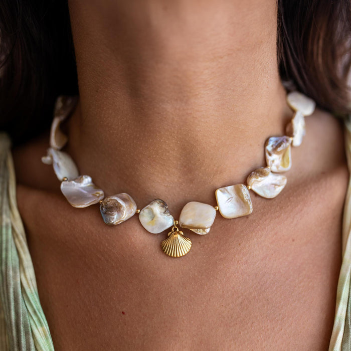 baroque pearl necklace with a gold shell pendant on a person's neck