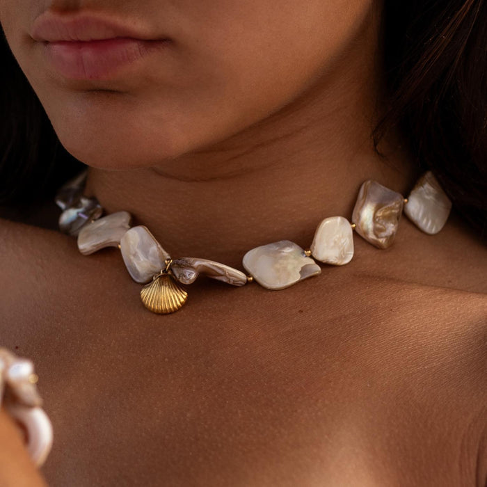 close up of a womans neck wearing a baroque pearl necklace with a gold shell pendant