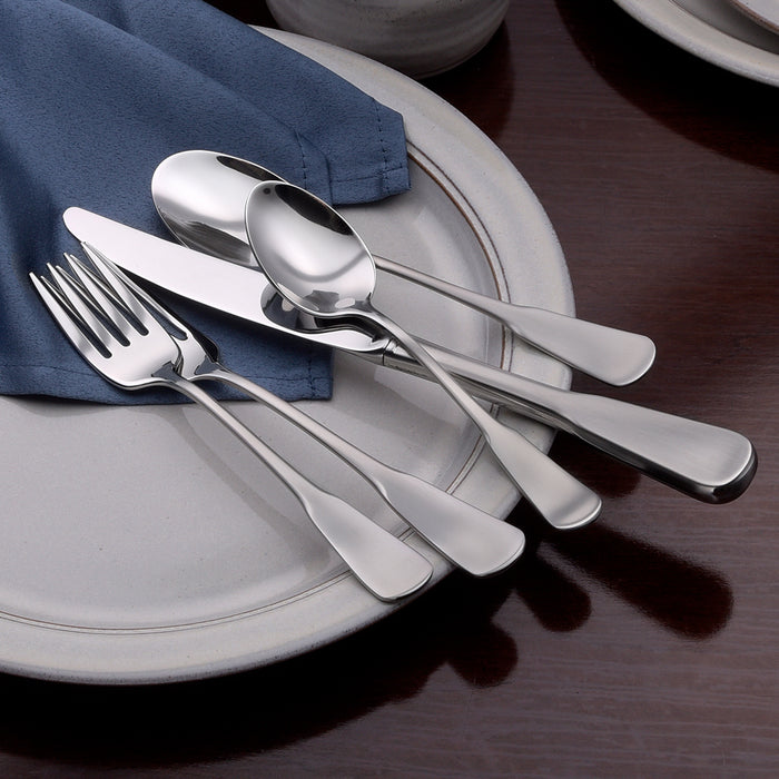 Angled top view of Candra 45-piece flatware set showing brushed handles and mirror bowls on a gray plate with a navy napkin