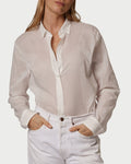 Woman wearing a light-colored shirt and white pants against a plain background