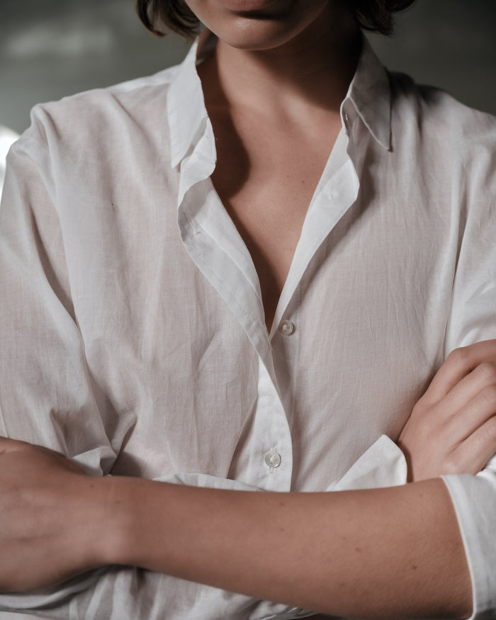 Person wearing a white button-up shirt with arms crossed, blurred background