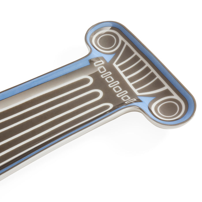 A close-up of a metallic decorative emblem or badge with a stylized classical column design, featuring a silver-gray body, white engraved lines, and a light blue border on a white background.