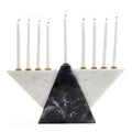 A three-tiered triangular Hanukkah menorah made of white and black marbled stone, holding nine white candles with gold-tone holders, set against a solid white background.