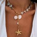 A gold waterproof necklace with baroque pearls, a starfish pendant and shell charms, displayed on a person's neck.
