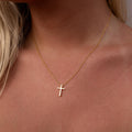 Gold necklace with a simple cross pendant on a person's neck