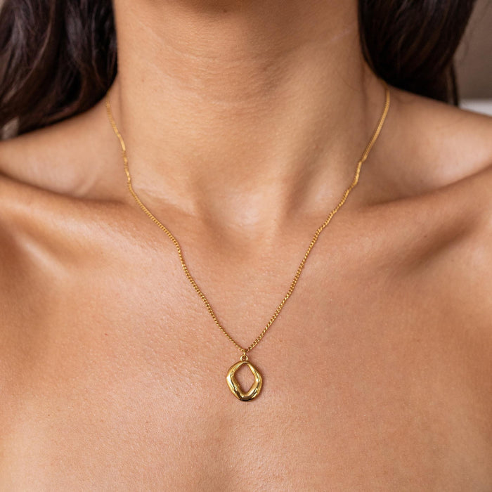 A dainty gold necklace with a geometric circle pendant worn by a woman.
