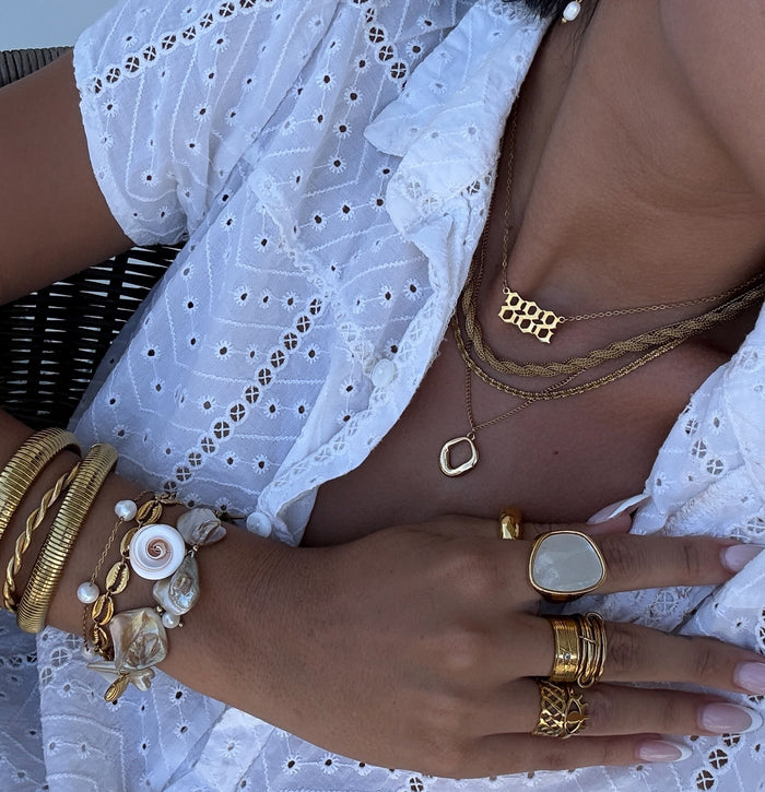 Close-up of a person wearing gold jewelry including bracelets, necklaces, and rings on a white lace outfit.